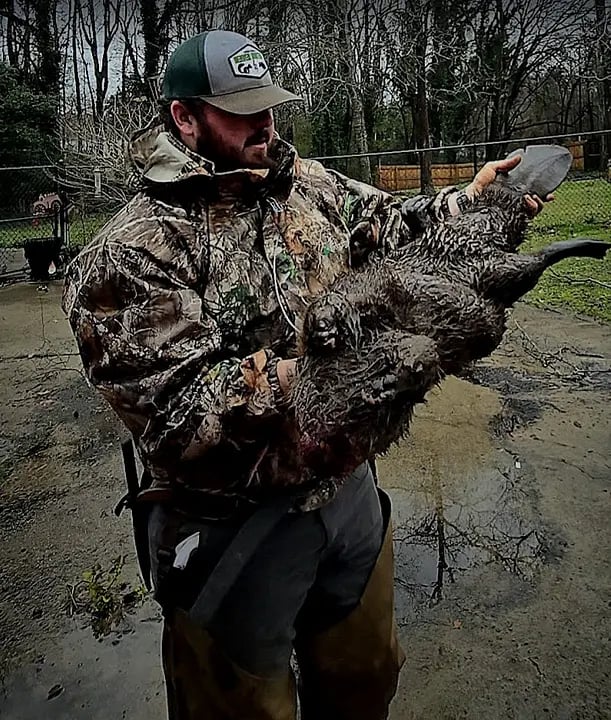 Person in camouflage holding a large wild turkey outdoors