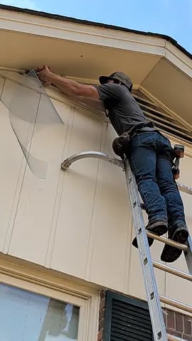 Worker on ladder repairs exterior of house under blue sky