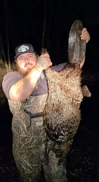 Hunter holding large furry animal at night in camouflage clothing